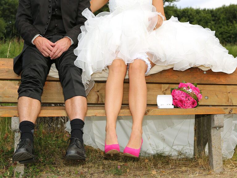 Ein Brautpaar sitzt auf der Lehne einer Bank wobei ihre Gesichter nicht zu sehen sind