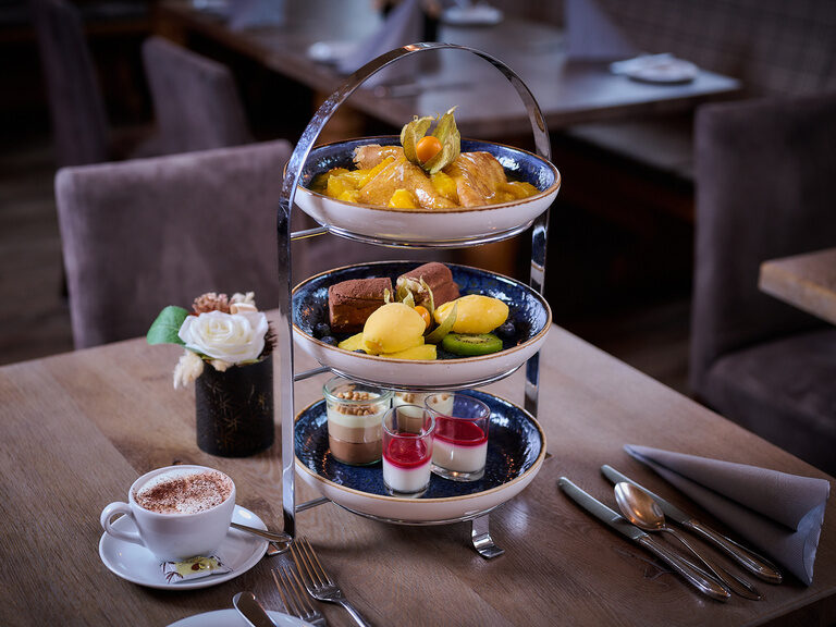 Eine sogenannte "Dessert-Etagere" steht auf einem Tisch im Hotel am See neben einer Tasse Kaffee