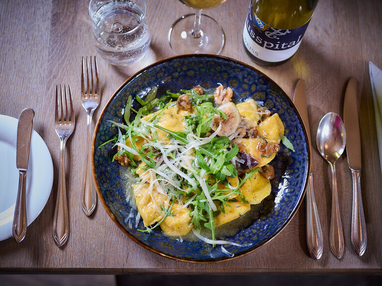 Ein Teller Ravioli mit Pecorino-Feigen-Füllung steht auf einem Tisch mit Besteck
